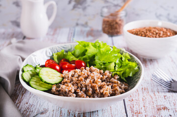 Bowl with buckwheat, cucumber, cherry tomato and lettuce on the table for a healthy lunch