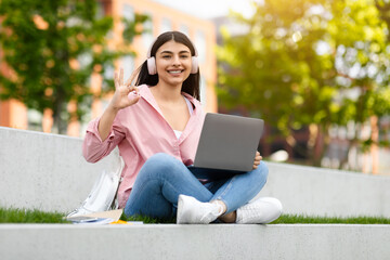 Happy young student signaling peace with laptop