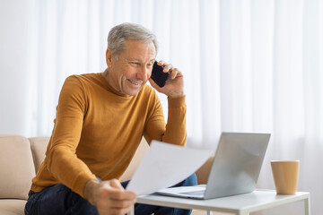 Elderly man analyzing documents with a phone call
