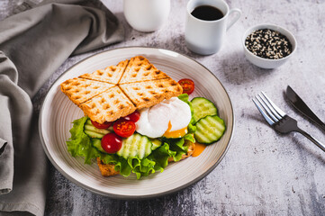 Poached egg with cucumber, cherry tomato and lettuce on waffle toast on a plate