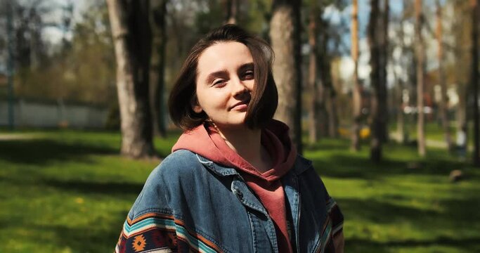 Portrait of happy young woman in spring sunlight. Cheerful young adult hipster female in park