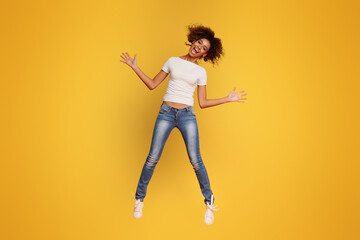 Cheerful african girl jumping in air, orange background