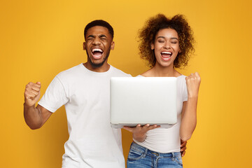 Excited black couple celebrating win with laptop