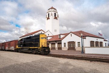 Yellow locomotive races past a train depot