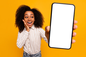 Excited woman presenting smartphone screen on yellow