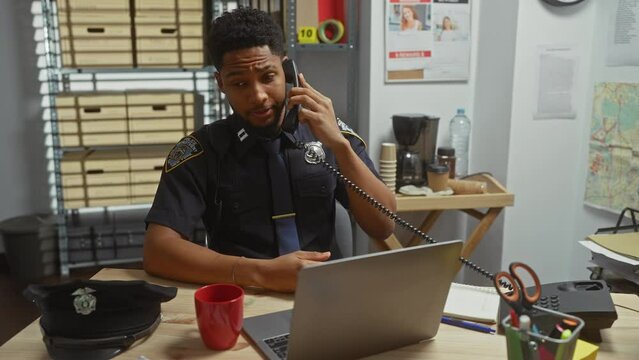 African american policeman in uniform discussing a case on the phone in a cluttered office setting.