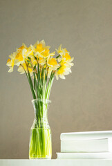 Vertical image. Fresh bouquet of spring yellow flowers and books against empty wall