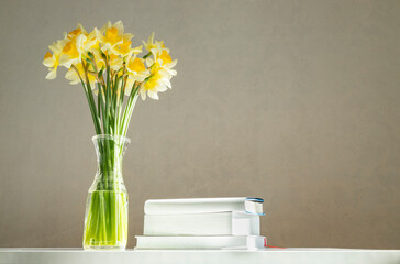 Stack of books and vase full of fresh beautiful daffodils against white wall. Joy of reading
