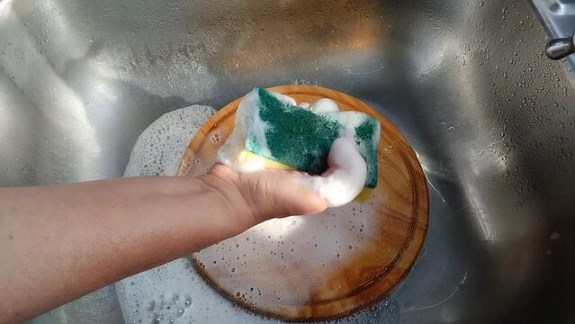 Una mano de mujer que presiona una esponja amarilla  llena  de jab&oacute;n l&iacute;quido  en un fregadero