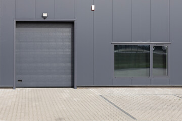 Gray industrial wall with roller shutter door and window. Modern Industrial Building Facade
