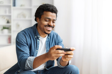 Smiling Black Man Playing Games On Smartphone in Bright Indoor Setting
