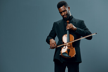 Talented African American man in suit playing the violin beautifully on a neutral gray background