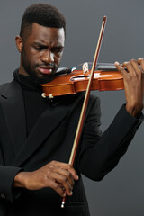 African American man in black suit playing violin on gray background in elegant and passionate musical performance