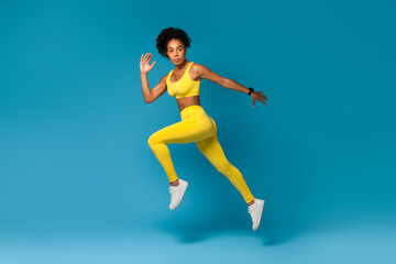 Fototapeta na wymiar Athlete captured mid-air in yellow sportswear on blue background