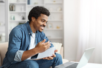 Smiling Black Man Engaging in Video Call on Laptop in Bright Home Office