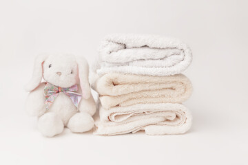 Bunny fluffy toy with clean baby beige soft bath towels stack on a white background