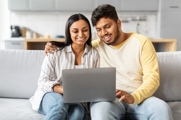 Indian Man and Woman Sitting on a Couch Looking at a Laptop