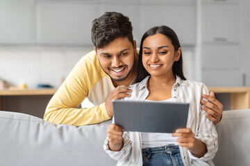 Indian Man and Woman Sitting on Couch Looking at Tablet