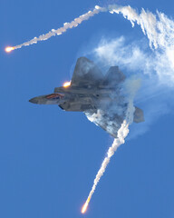 Epic view of a F-22 Raptor deploying flares in a turn, in smoke and in beautiful light