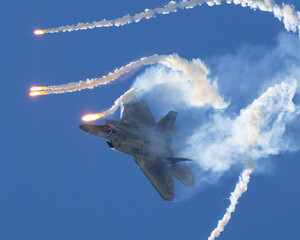 Epic view of a F-22 Raptor deploying flares in a turn, in smoke and in beautiful light