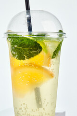 Lemonade with lemon, orange, lime and mint in transparent plastic glass on white background