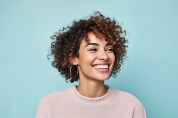 A woman with curly hair is smiling and wearing a pink sweater