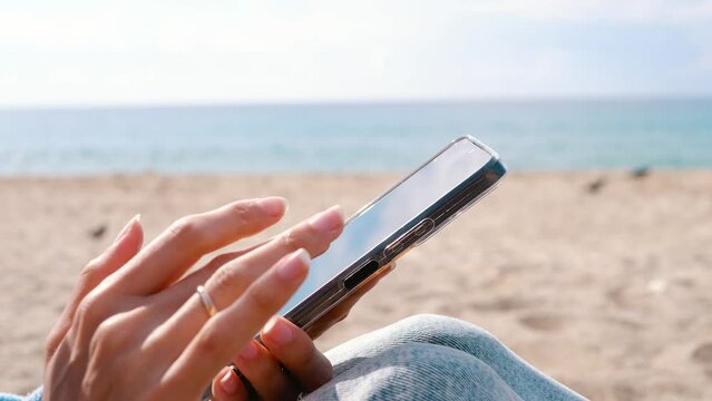 a woman's hand holds a phone. Beach and sea in the background