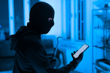 Thief using a smartphone during a break-in - obrazy, fototapety, plakaty