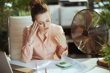 unhappy modern female worker at work with electric fan