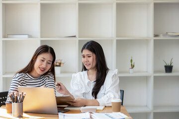 Two cheerful businesswomen brainstorming and sharing ideas in a collaborative workspace, with a laptop and coffee on the table.