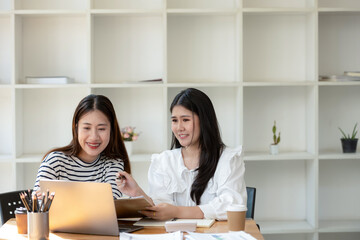 Two cheerful businesswomen brainstorming and sharing ideas in a collaborative workspace, with a laptop and coffee on the table.