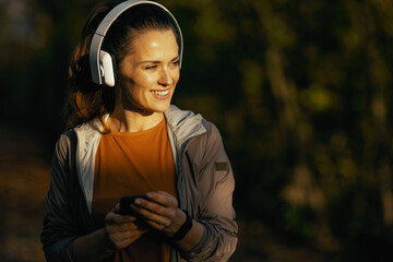 happy stylish woman in park listening to music with headphones