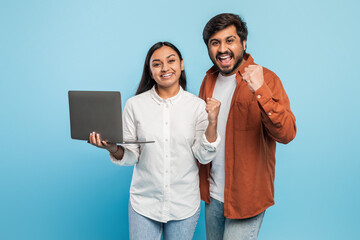 Excited couple with laptop celebrating success on blue
