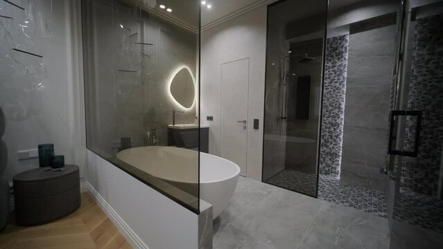 Sleek and modern bathroom viewed from a bedroom, showcasing an oval mirror with backlighting, a freestanding tub, and a walk-in shower with geometric tiles.
