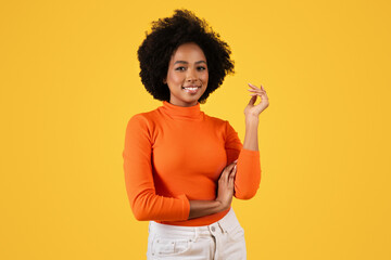 Confident African American woman with curly hair poses in a stylish orange turtleneck