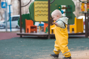 A beautiful, cheerful little boy of two years old walks on the playground in the spring. A child is playing with a shovel in the sandbox. The concept of parenthood, happy childhood and family.