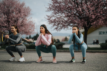 Outdoor exercise session with three women squatting synchronously on a street, promoting fitness...