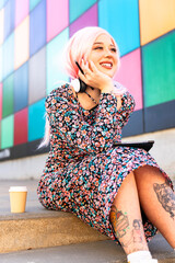 Modern girl with pink hair and headphones sitting on the stairs in the faculty