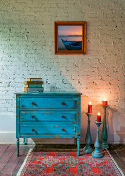 Studio shot of retro composition of Green vintage cabinet, candlesticks with lighted candles and hanged painting on white bricks wall