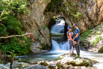 Family standing on rock with scenic view of majestic waterfall cascade of Bodentaler Felsentor, Tscheppaschlucht, Loibl Valley, Karawanks, Carinthia, Austria. Water cascading down cliff face into pool