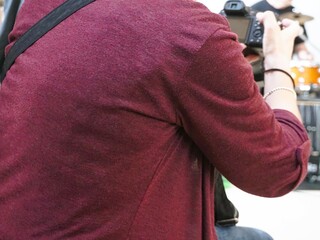 Sitzende Frau mit weinroter Strickjacke hält Fotocamera in Hand 