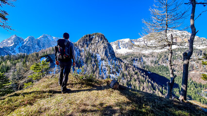 Fototapeta na wymiar Hiker man enjoying scenic view of Karawanks mountain range in Carinthia, Austria. Looking at snow capped summit of Vertatscha and Hochstuhl. Remote alpine landscape in Bodental, Austrian Alps