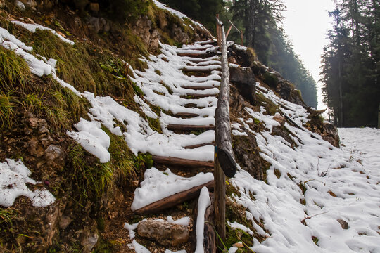 Steep snow covered hiking trail through forest in mountain ranges of Karawanks, Carinthia, Austria. Wooden slippery stairs due to ice cover. Cold morning in alpine landscape in Bodental Austrian Alps