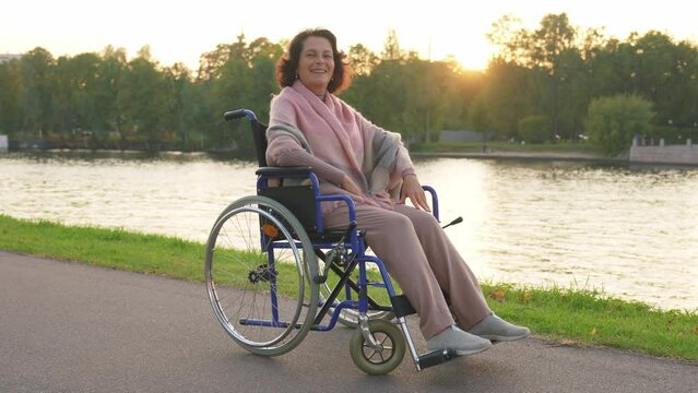 Happy senior woman in wheelchair smiling enjoying freedom walking on road in city park outdoor. Old cheerful positive woman in chair for people with disability. Disability disease rehabilitation