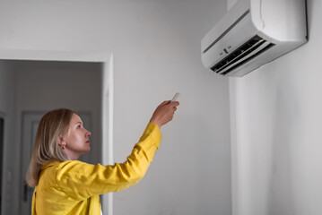 Woman holding remote control aimed at the air conditioner.