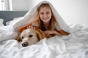 Girl Lies Under Blanket With Her Golden Retriever Dog - obrazy, fototapety, plakaty