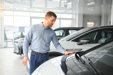 Concept of buying electric vehicle. Handsome business man stands near electric car at dealership