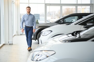 Concept of buying electric vehicle. Handsome business man stands near electric car at dealership