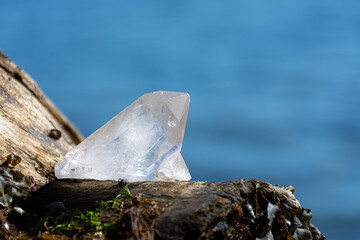 A close up image of a clear quartz crystal with a blue ocean background. 