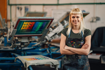 Confident print shop worker near screen printing press smiling at camera